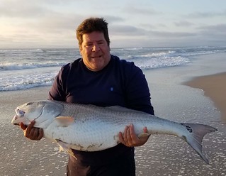 Photo of a man on the beach holding a large red drum. 