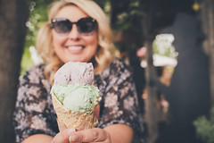 Lifestyle portrait of a young blond woman enjoying a waffle cone. Focus on ice cream cone, woman intentionally blurred