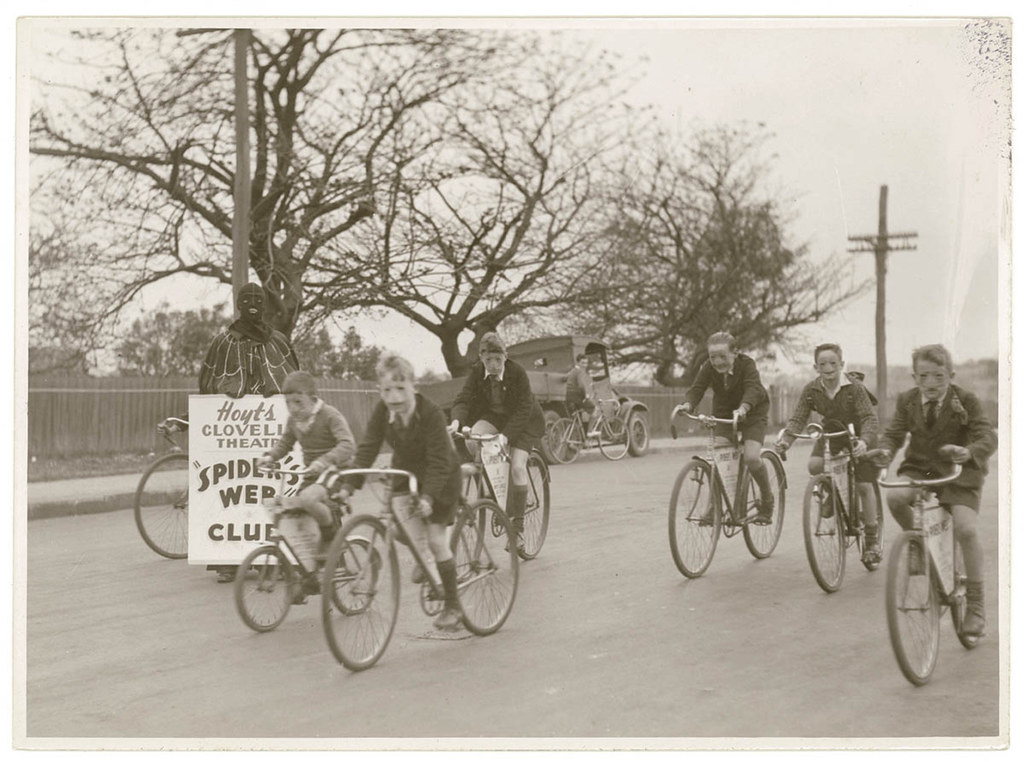 NSW Boys of Hoyts Clovelly Theatre Spider's Web Club ride their bikes while Spiderman looks on. Clovelly, NSW, Australia 1936