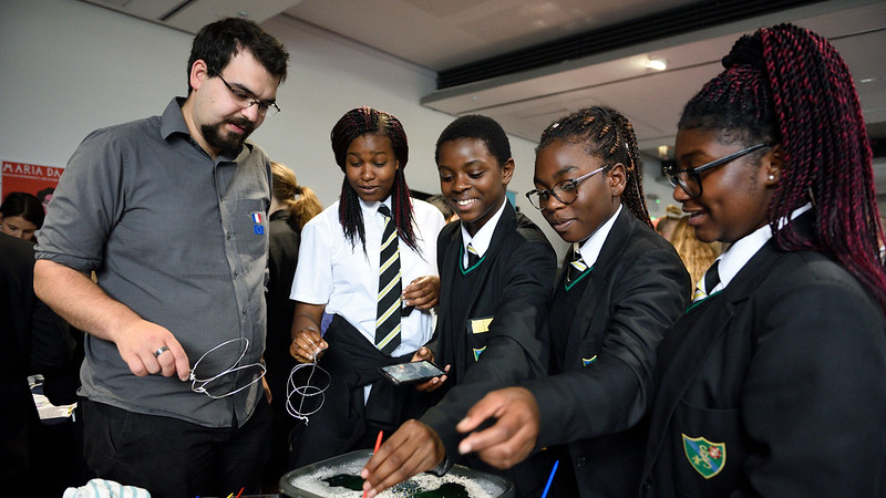 A researcher explaining a science demonstration to three school students