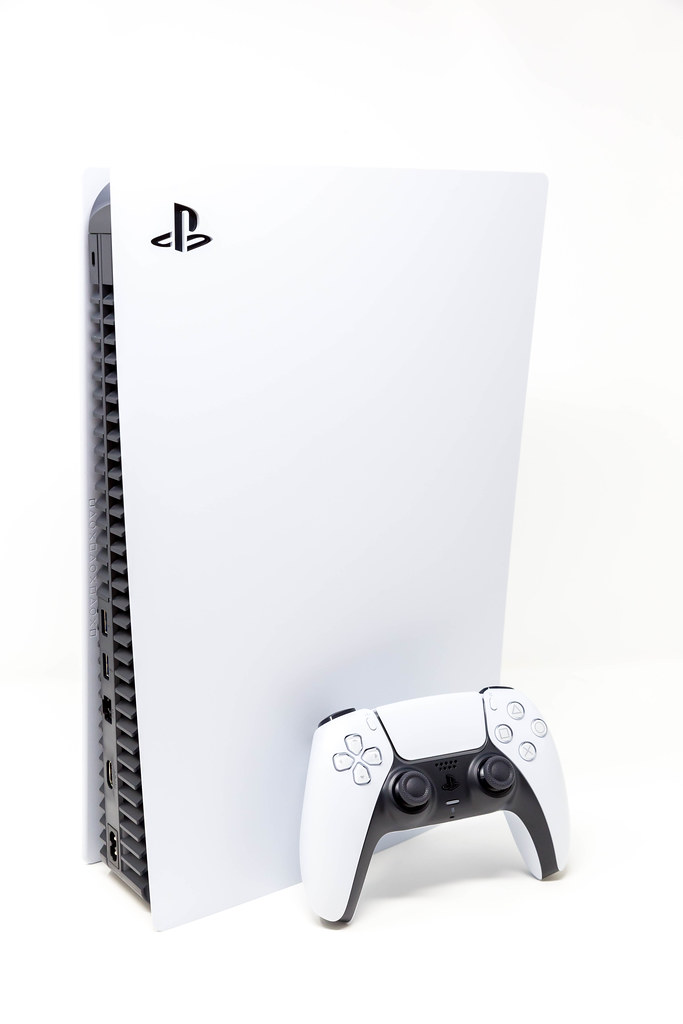 Sony DualSense Wireless Controller leaning on a standing Sony PlayStation 5 Digital Edition on White Background