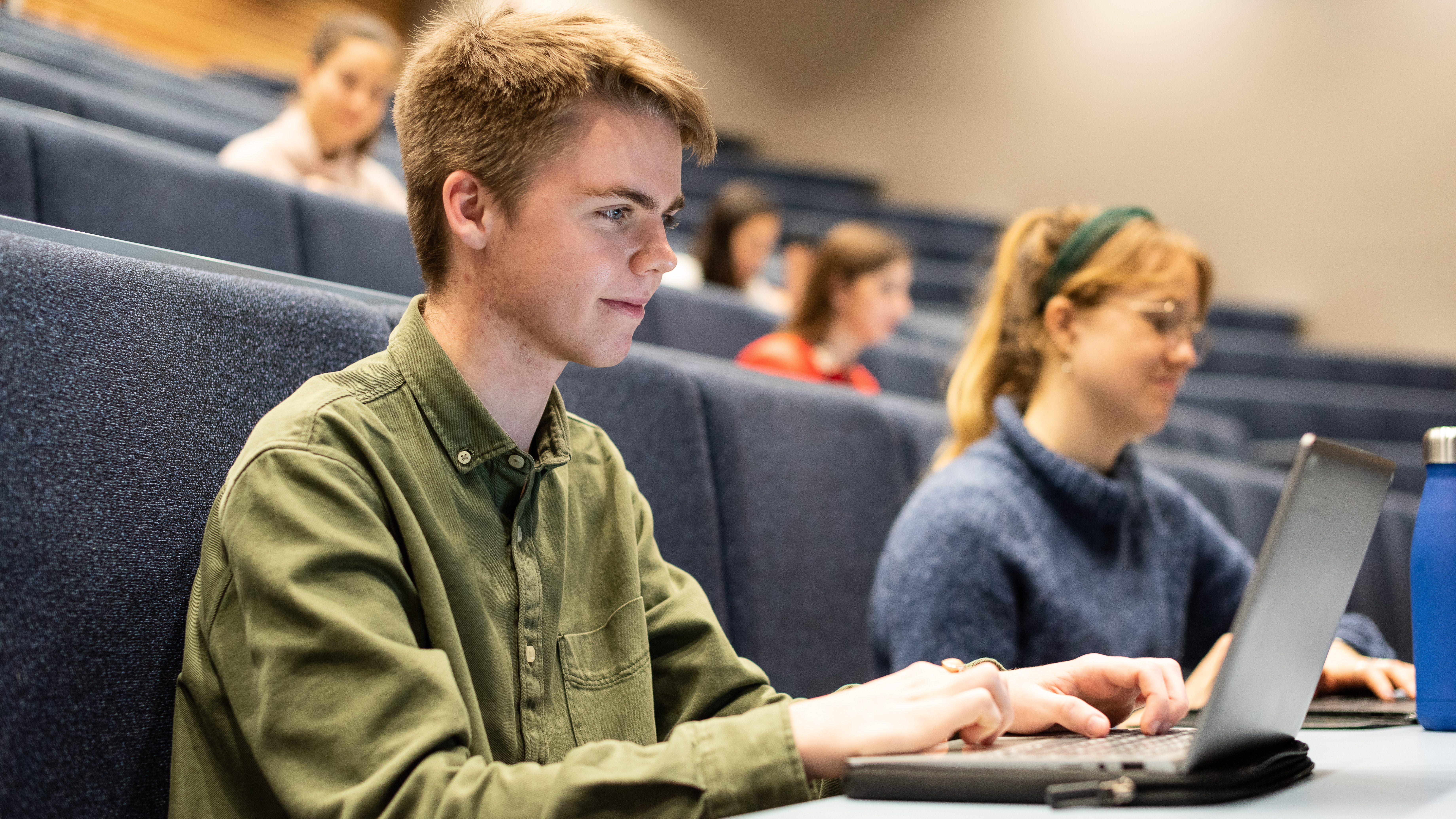 A young man using a laptop computer in a lecture hall at university.