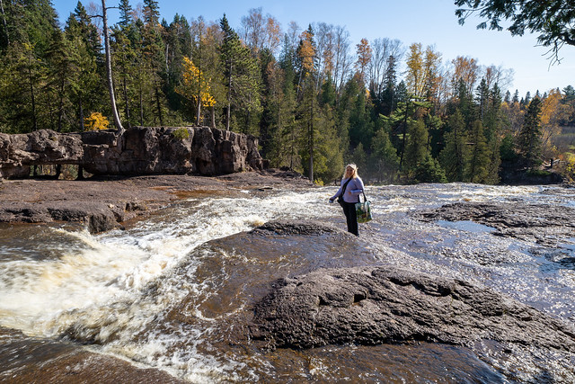 Cute woman tourist takes photos by standing in the middle of the Gooseberry River at Gooseberry Falls State Park in Minnesota