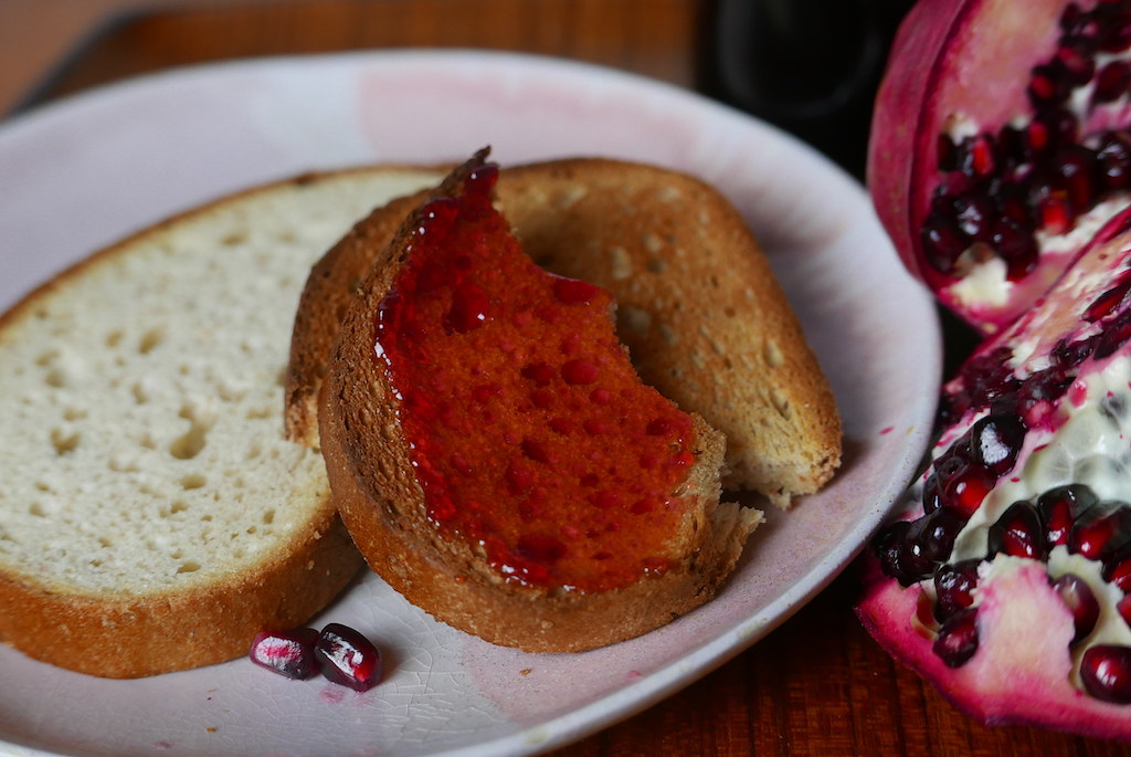 Canning Recipes Post: Pomegranate jelly on toast next to a halved pomegranate. 