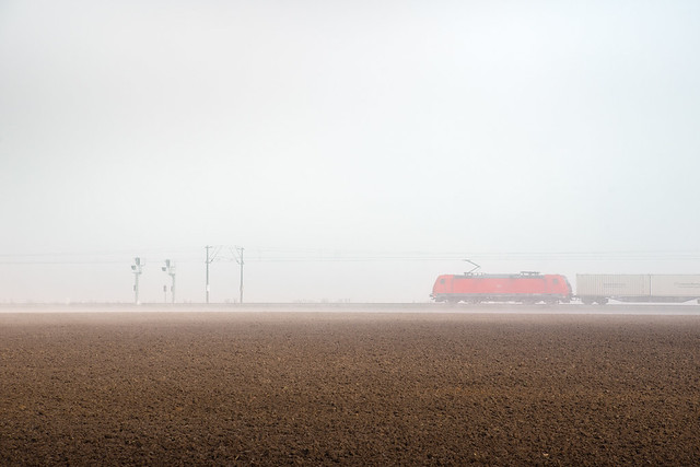 A Red Train Crosses the Foggy Plain
