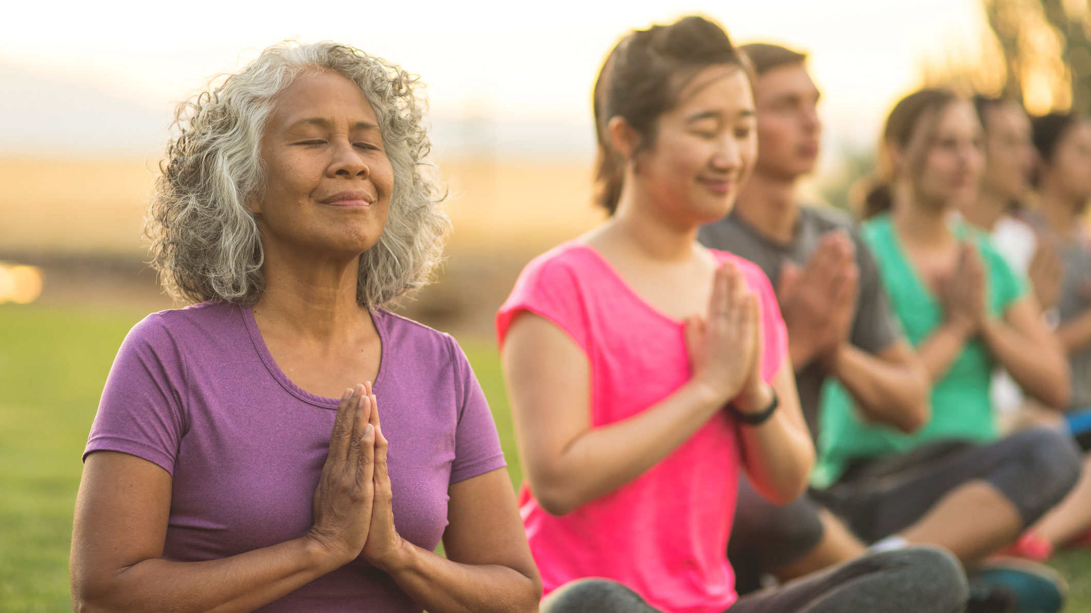 A row of adults sitting in a line with their hands together doing yoga