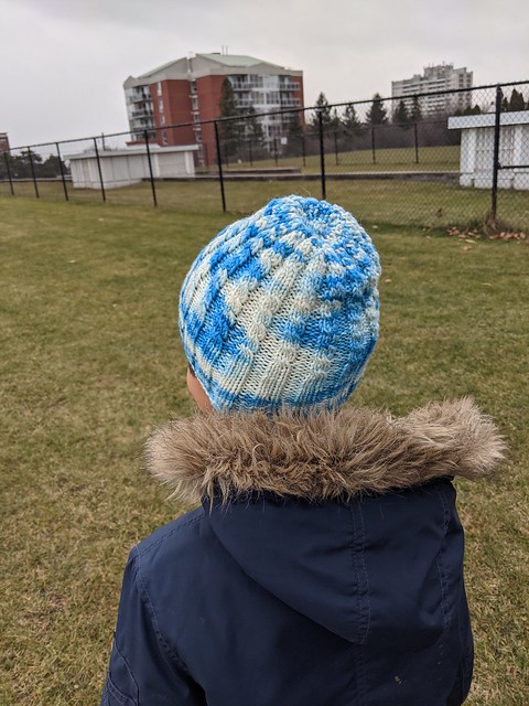 Child wearing cable knit hat by irieknit in Rhichard Devrieze denim-E colourway yarn.