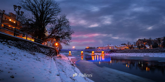 uzhhorod, ukraine - 26 DEC 2016: winter cityscape at dawn. beautiful scenery on the river uzh. city lights reflecting in the water. snow on the embankment