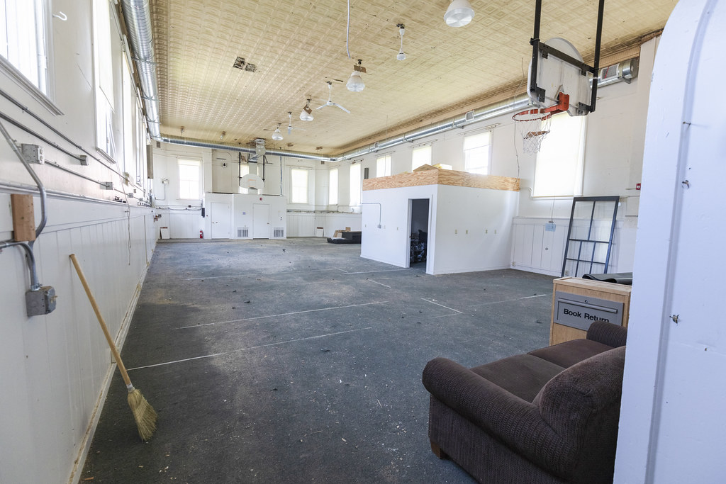 The interior of a building with tall ceilings, concrete flooring, and basketball hoops on either end of the room.