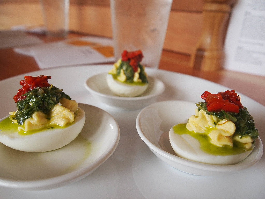 Three deviled eggs, each on its plate, topped with a green salsa and red roasted peppers.