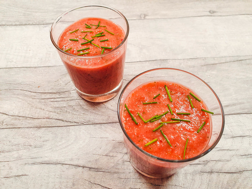 Two glasses with the vegetarian Spanish tapas gazpacho, a red cold soup with green chopped chives on top.