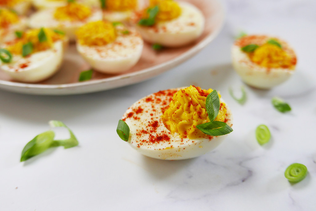 A deviled egg sitting on white marble with smoked paprika and green onion.