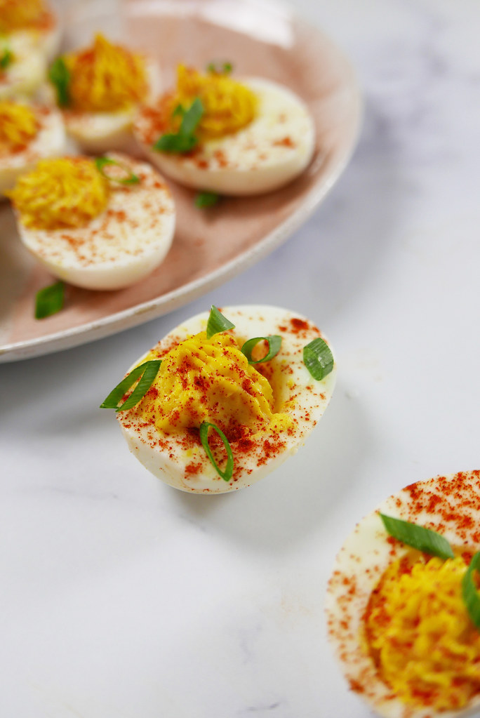 A shot of a deviled egg on a white marble counter. The egg is topped with smoked paprika and green onions. 