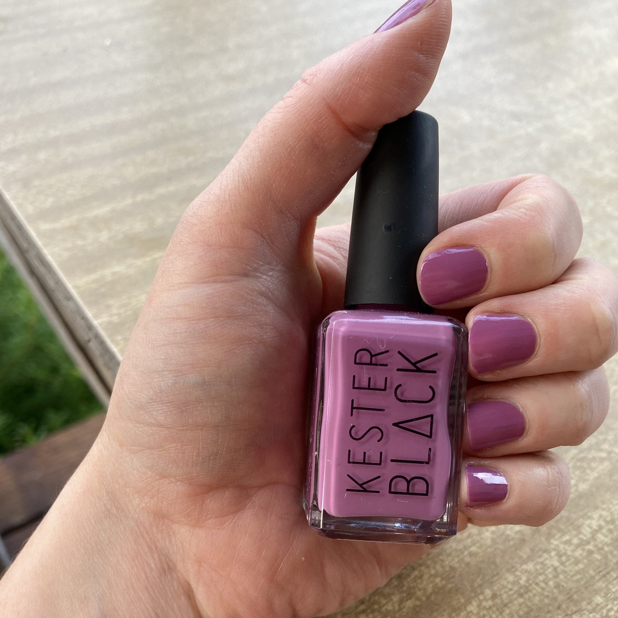 a white hand with purple painted nails, holding a bottle of 'kester black' purple polish