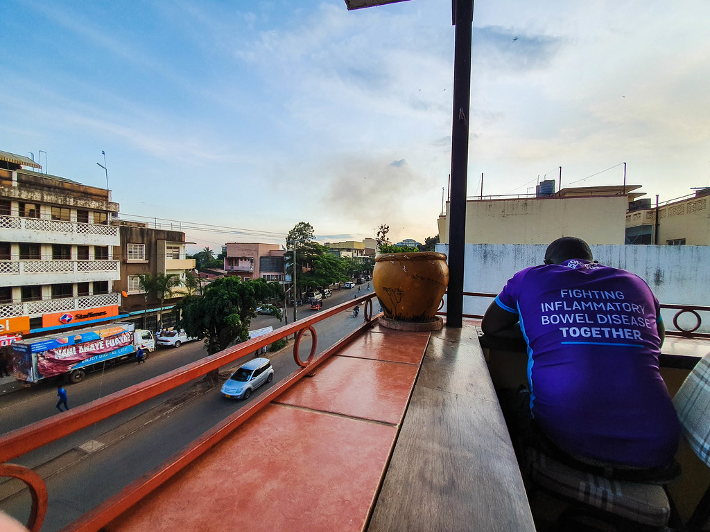 A man wearing a purple tshirt, looking down over the railing of the terrace