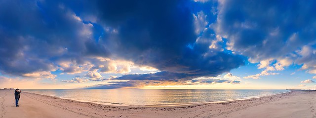 Dramatic natural landscape: cold leaden clouds reflecting in the sea, the skyline and a man standing on the sand (Panoramic landscape)