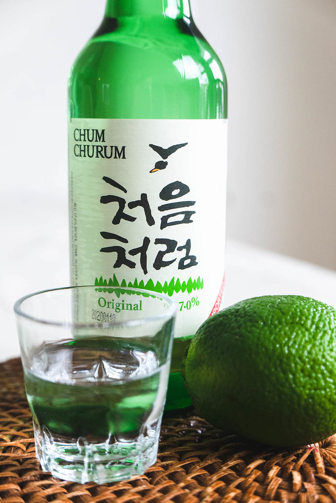 A close-up shot of a bottle of soju and a shot glass filled with soju. They sit next to a green lime. 