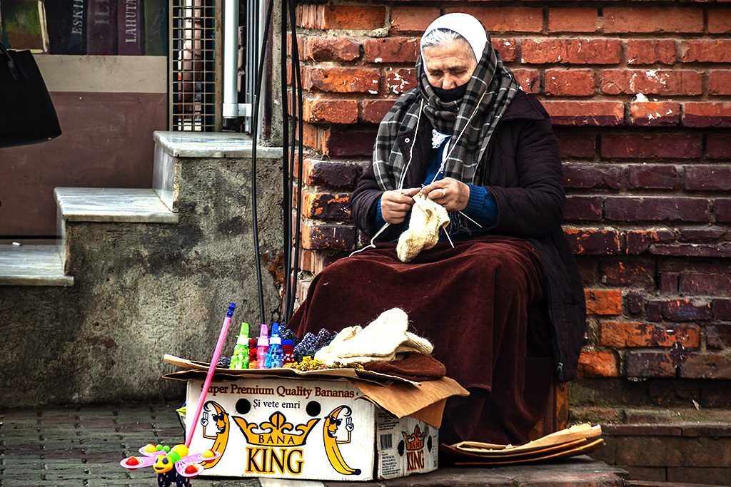 Old woman selling knitted caps and mittens on sidewalk on 3-6-21--Tirana