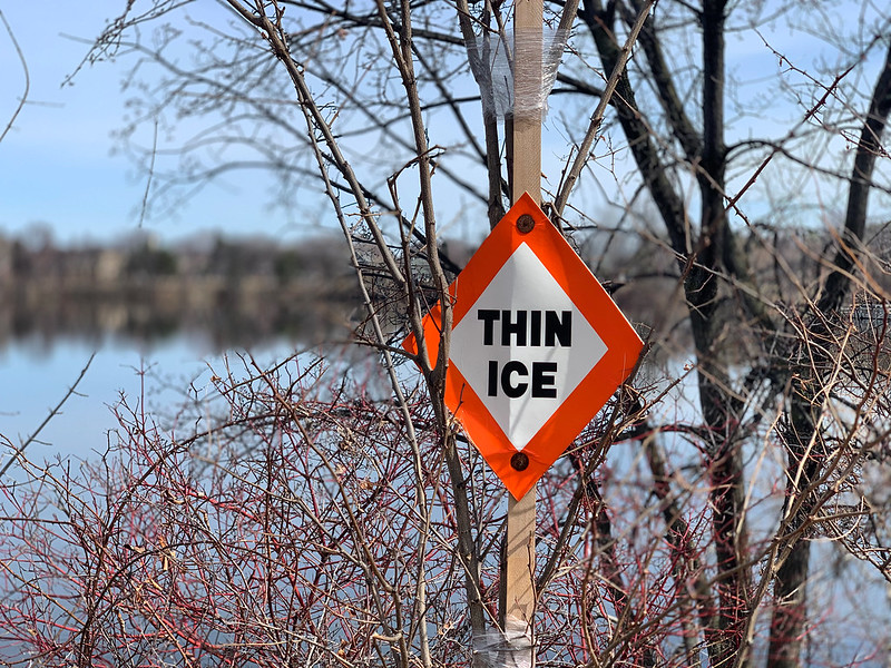 THIN ICE signage next to a fully melted Como Lake