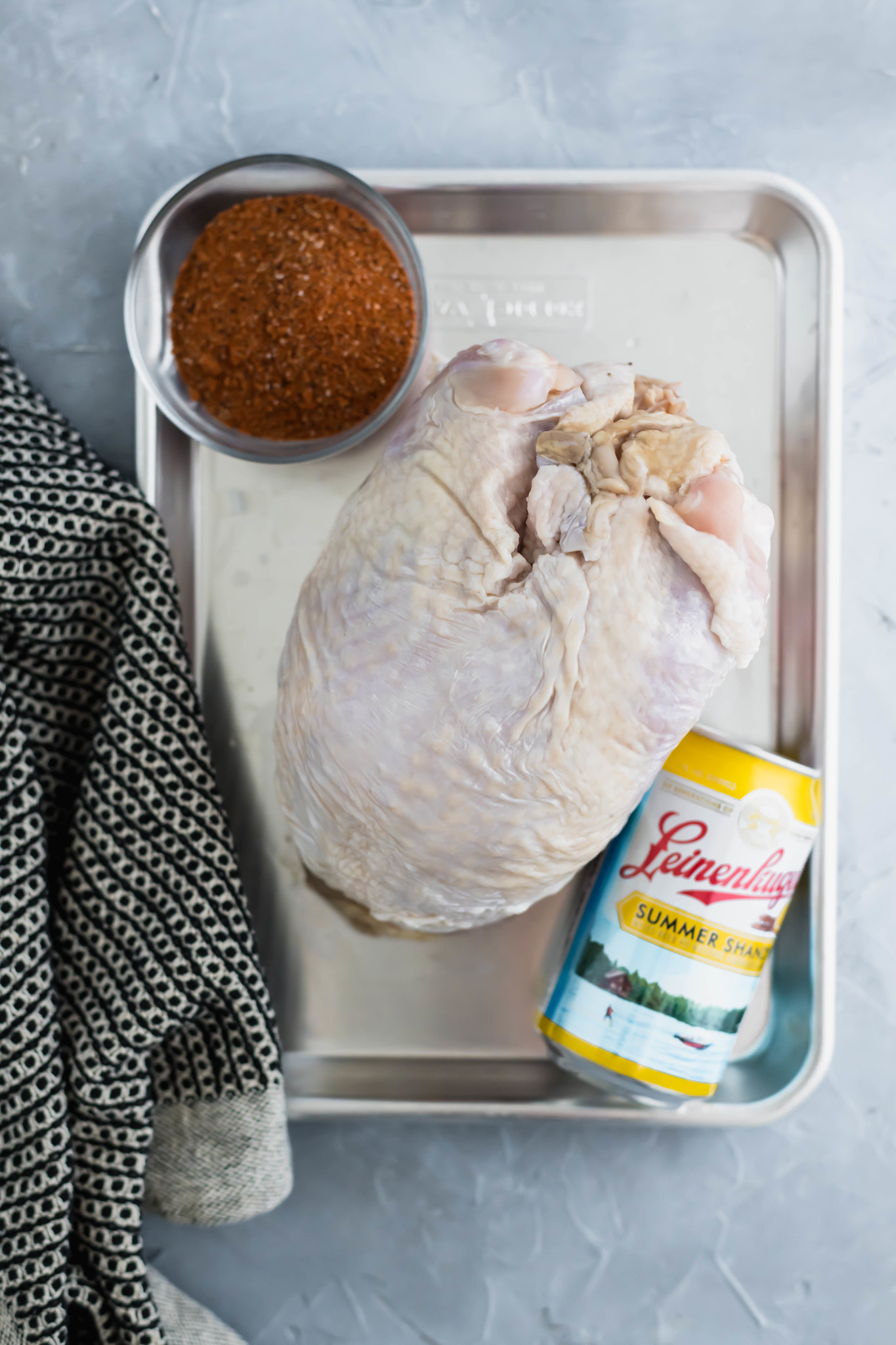 raw bone-in turkey breast, bbq rub and a can of beer on a metal tray