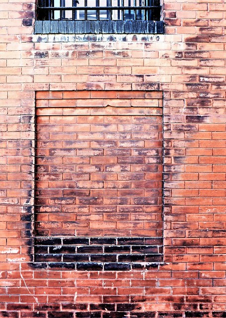 Bricked window under a barred window.  An aging wall.