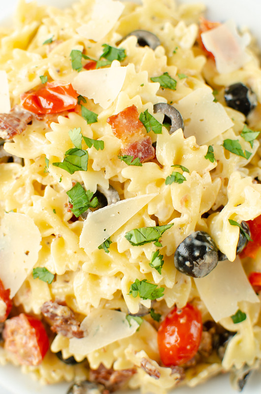 close up of pasta salad with parmesan cheese, black olives, tomatoes, and herbs