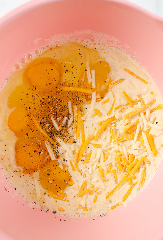 Eggs, milk, cheese, and black pepper in a red mixing bowl