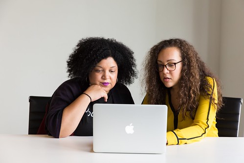 Two female presenting individuals working on a project on an apple laptop - 10 Technology Jobs that Don't Require a Four-Year Degree
