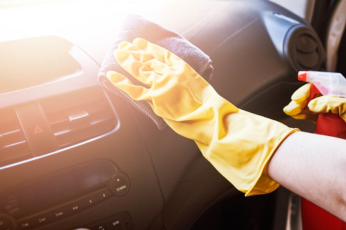 Someone wearing yellow rubber gloves cleaning the dashboard of a vehicle