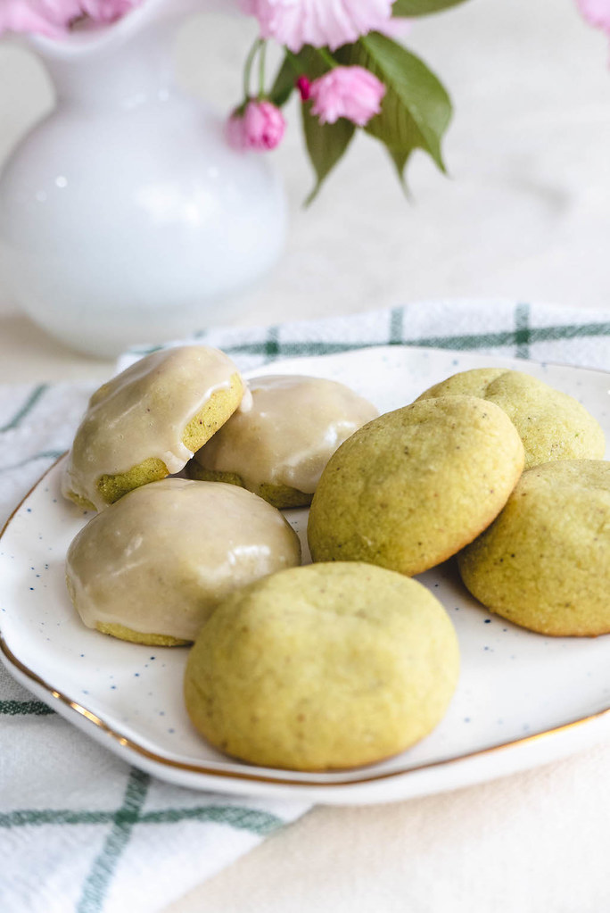 A side shot of pistachio butter cookies on a plate with flowers in the background.