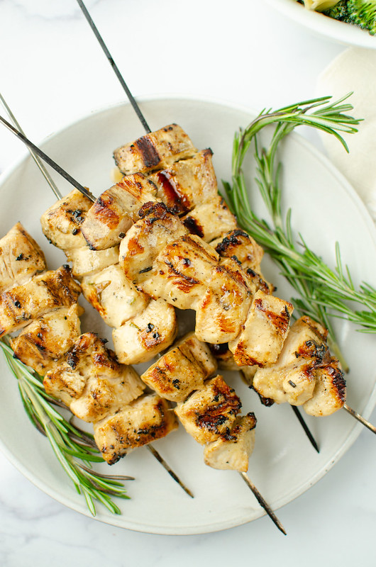 Overhead shot of four grilled chicken kabobs on a white plate with rosemary garnish