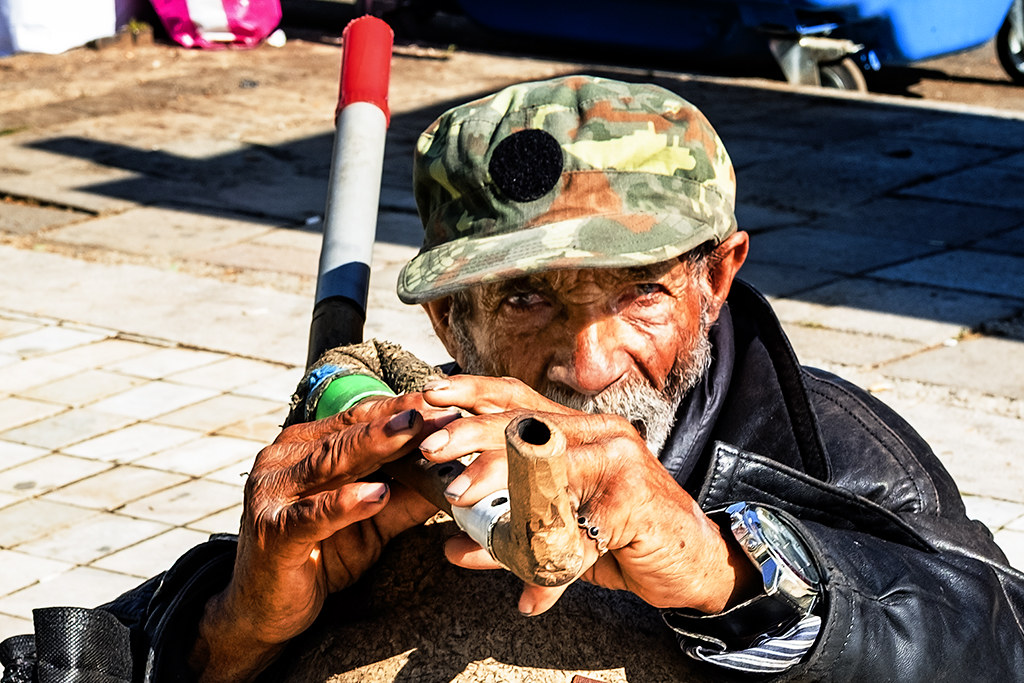 Man playing some homemade wind instrument on 4-15-21--Tirana (detail)