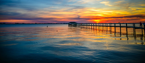 panoramic view sunset over indian river melbourne beach fl with fishing pier melbournebeach fla florida us usa america sun cloudy clouds water lagoon bay atlantic ocean orange red yellow blue calm