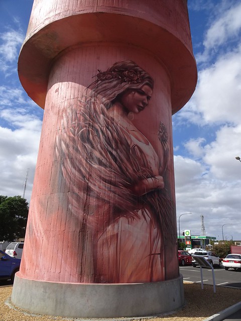 Kadina. Water tower art completed in 2017. A Celtic May Queen holds items of significance to the Cornish settled  district. A nugget of copper and a head of wheat. In a car park.