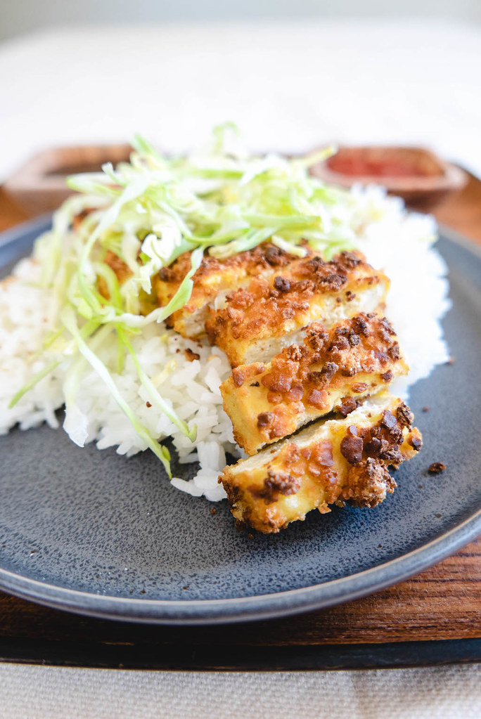 A side shot of tofu katsu over a bed of rice and topped with cabbage.