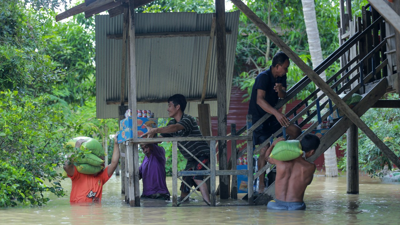 Men carrying food and supplies through flood water, before taking them up some stairs to store