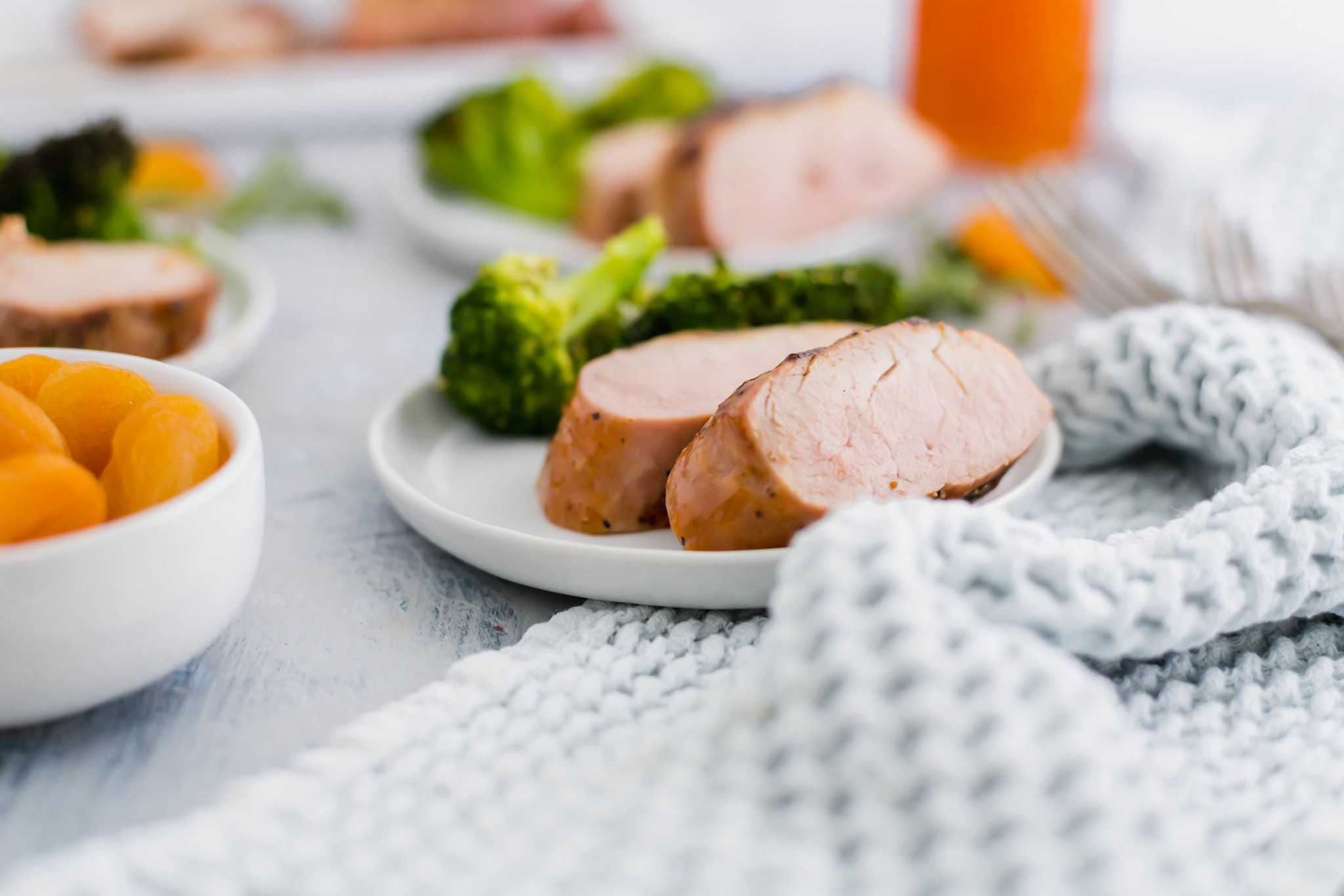 apricot glazed pork tenderloin slices on a small round white plate with roasted broccoli. Bowl of dried apricots on the side.