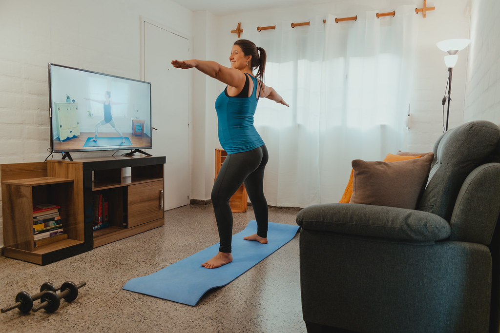 Pregnant Latin woman doing yoga and stretching at home while watching an internet class. Concept of exercise and healthy life at home.