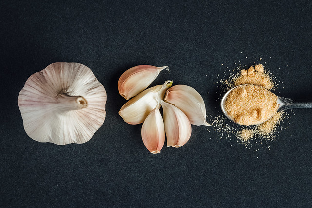 Garlic head, cloves of garlic and a teaspoon of garlic powder on black background