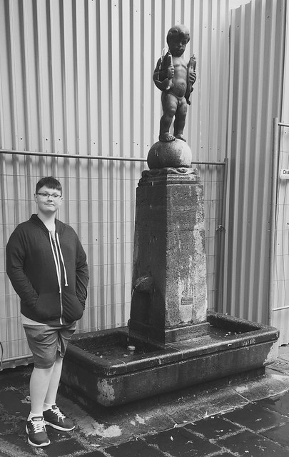 My grandson standing beside the statue in Aachen located to the side of a street near the Aachener D.o.m. , photograph converted to black and white , Martin’s photograph , Aachen , Germany , June 9. 2019
