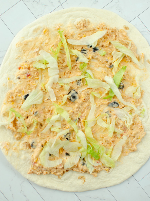 Flour tortilla spread with cream cheese, seasoned taco meat, salsa, cheddar cheese, black olives, and shredded lettuce