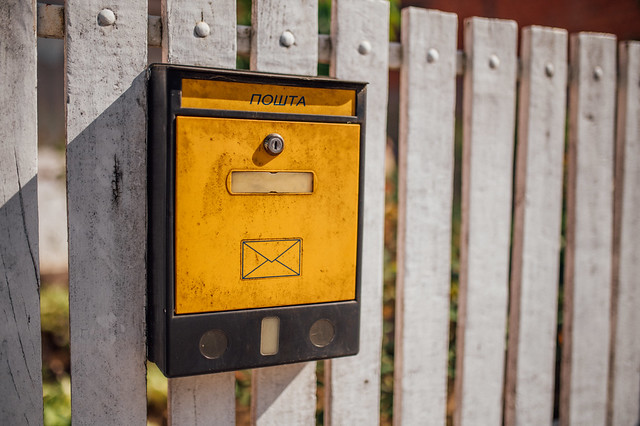 Close-up of a yellow mailbox attached to a wooden fence