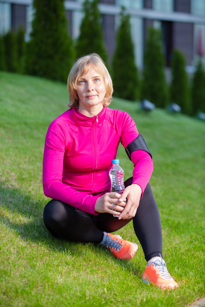 Tranquil Mature Caucasian Female in Sport Outfit Posing With Bottle of Clear Water While Resting Outdoors.