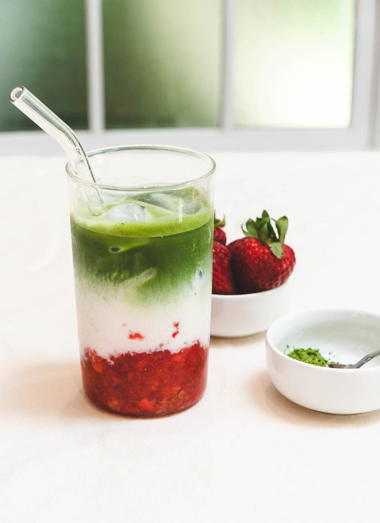 Iced strawberry matcha latte next to strawberries and matcha in a bowl.