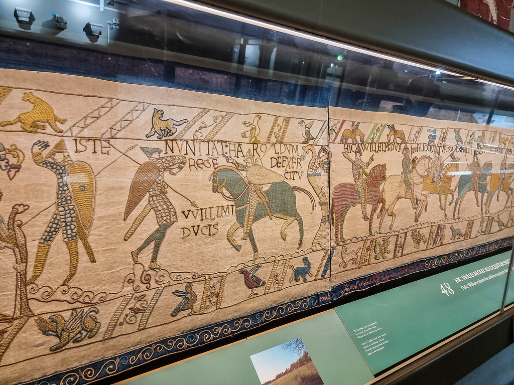 One segment of the copy of the Bayeux Tapestry displayed at Reading Museum, under a glass case, on the wall.