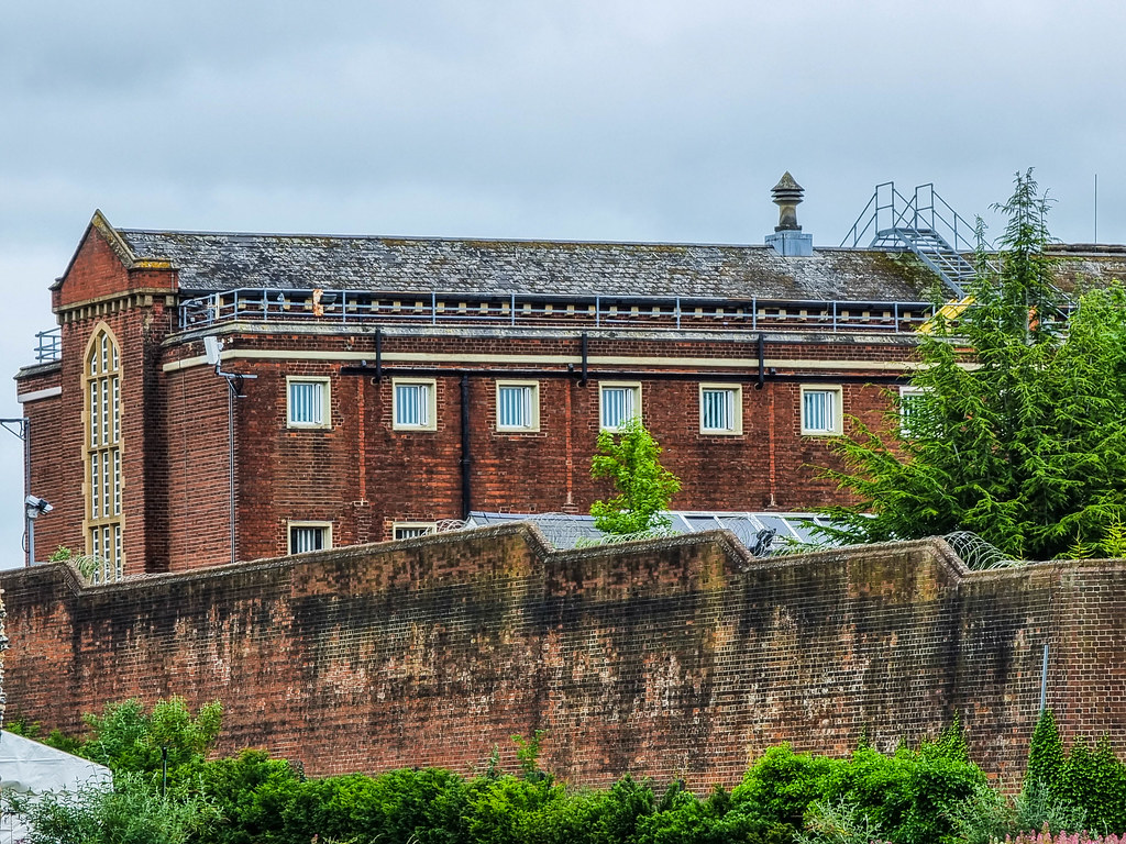 The former prison of Reading, made from red bricks, with a tall wall in front. On top of the wall there is spike wire. Behind the wall you can see the top floors of the prison, there Oscar Wilde's cell used to be.