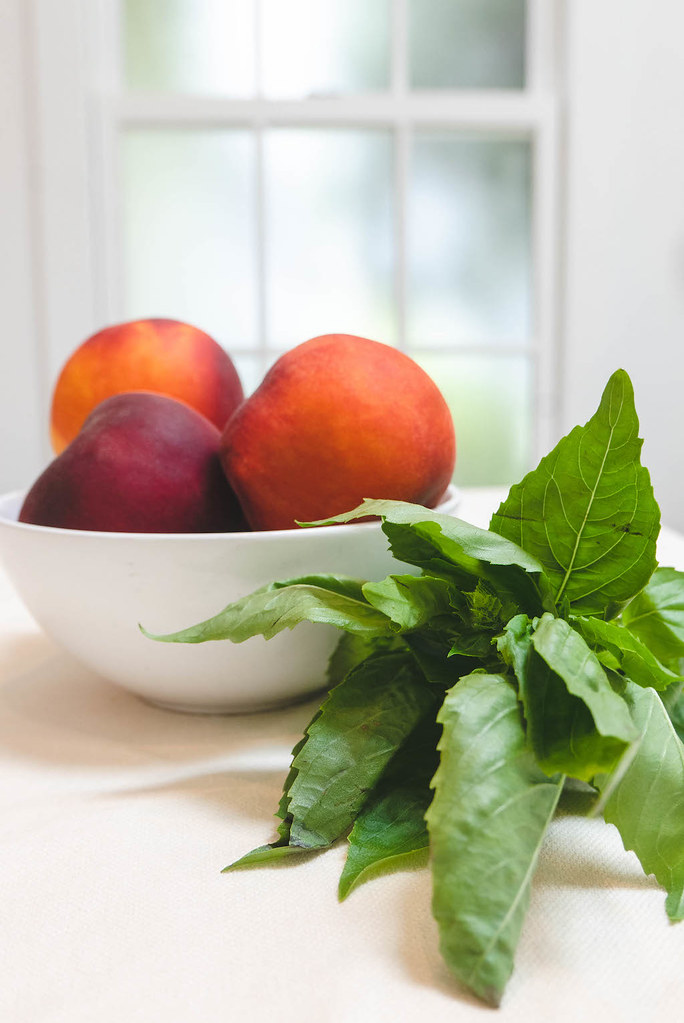 A bowl of peaches next to a bunch of basil. 