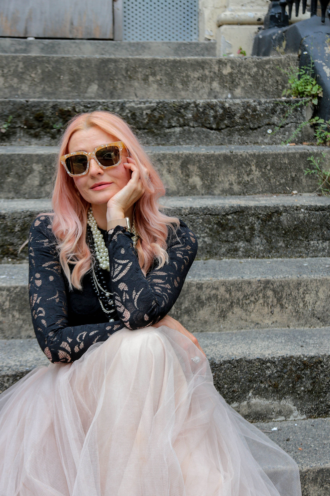 Catherine Summers AKA Not Dressed As Lamb | Wearing: cropped, long sleeve black lace top, pearl-effect square sunglasses, nude tulle maxi skirt, black lace-up boots | Sitting on the steps leading up to a boarded-up abandoned London town house