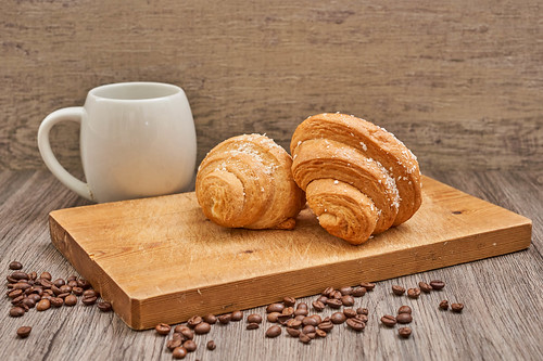 Coffee cup and raw coffee beans with tasty croissants on the wooden cutting board | by wuestenigel