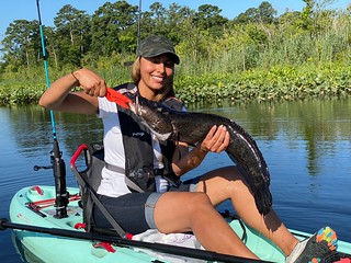 Photo of woman in a small boat holding a large northern snakehead